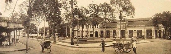 013a. Ludovic Crespin - Saigon đầu thập niên 1920: Place de l'hôtel de ville, boulevard Bonnard, boulevard Charner. Quảng trường tòa đô chính, góc đại lộ Bonnard (Lê Lợi) và Charner (Nguyễn Huệ). Chính giữa đường Lê Lợi là công viên, và có tượng của Francis Garnier nhìn về phía nhà hát thành phố. Bên phải hình là tiệm “Auto-Hall” bán các loại xe hơi. Bên trái hình là nhà hàng Pancrazi mở đến tối khuya (5). Những người kéo xe, phía phải hình, đang nhìn về phía người chụp ảnh (Crespin).