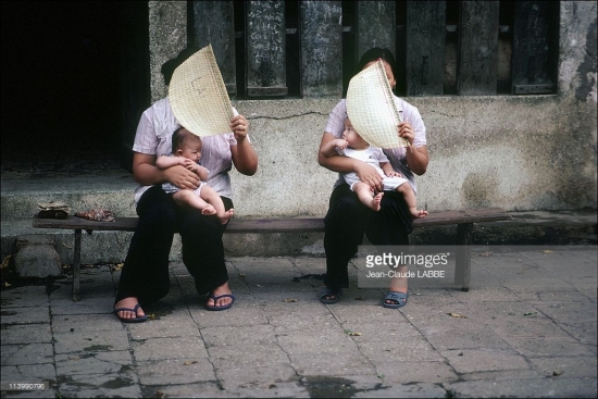 Hai người phụ nữ ngồi quạt cho con nhỏ trên vỉa hè.